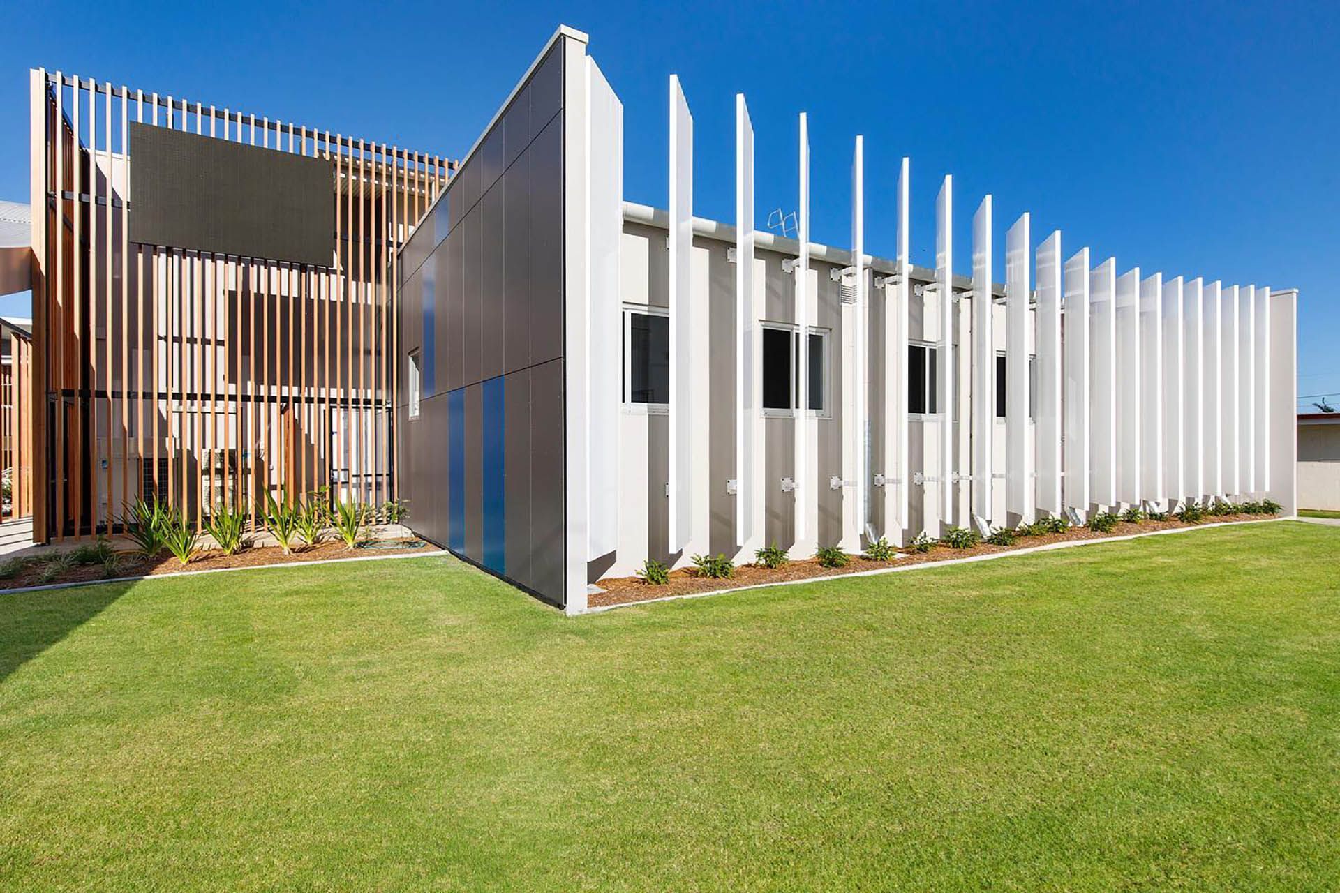 Modern white building with vertical slats and a green lawn under a clear blue sky