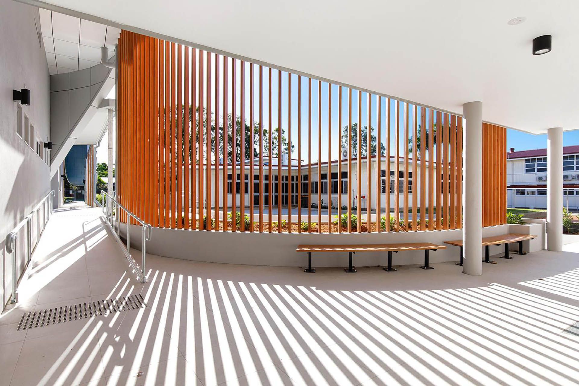 Modern building courtyard with orange vertical slats casting striped shadows on the floor