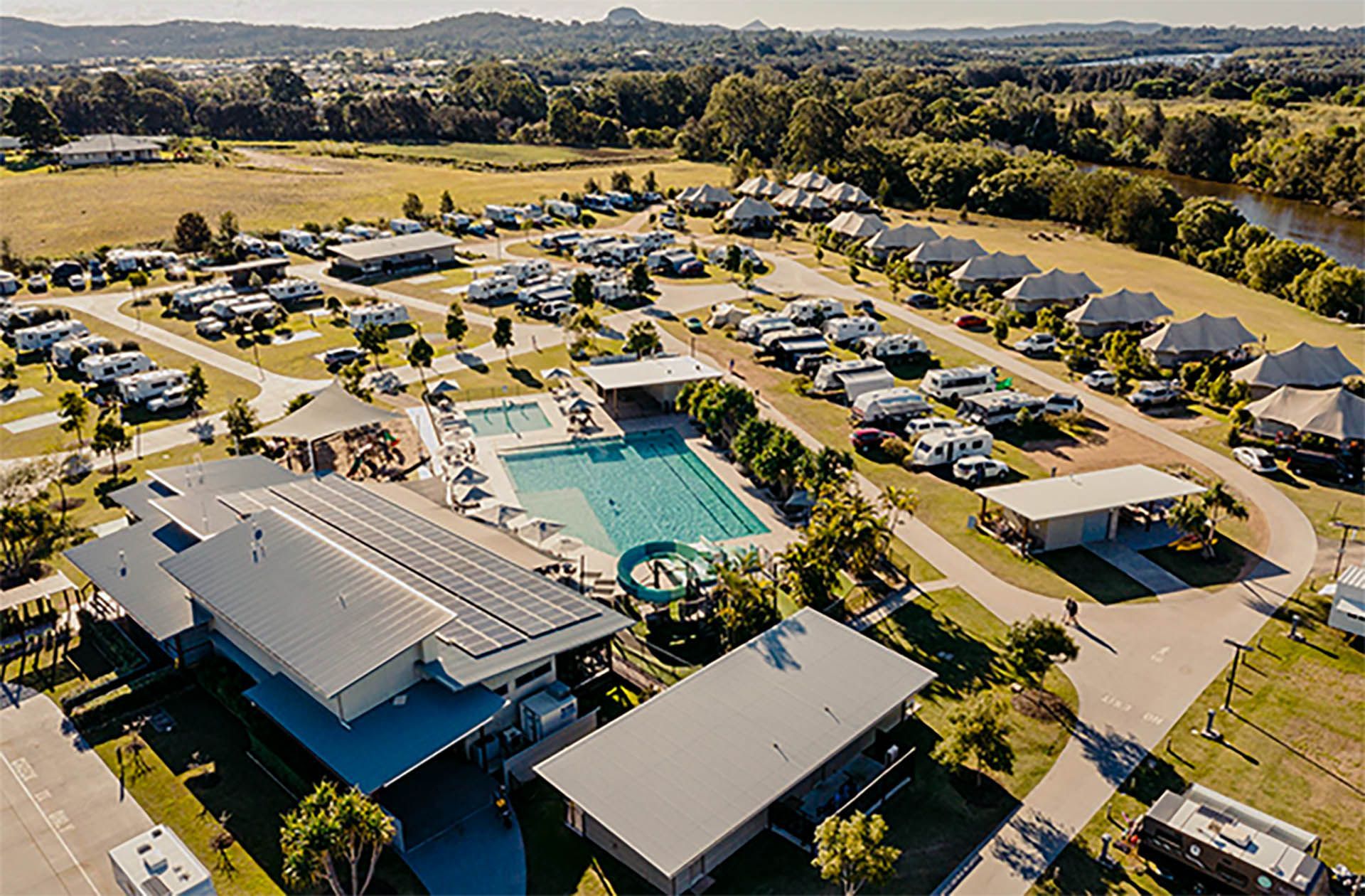 Aerial view of a resort pool and buildings surrounded by parked cars and trees