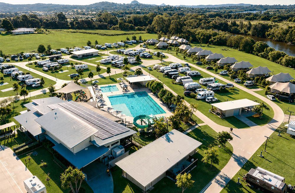 Aerial view of a sunny RV resort with pool, cabins, and green lawns surrounded by trees