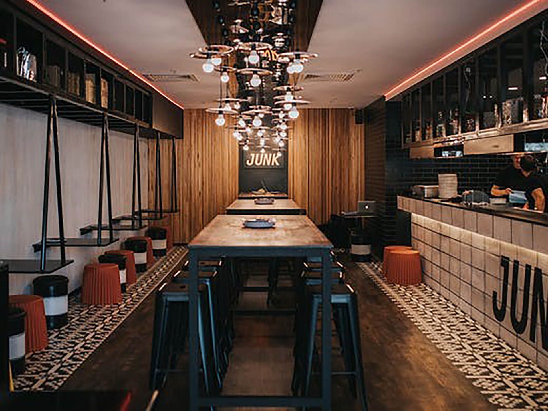 Modern bar interior with long wooden tables, stools, shelves, and warm ambient lighting