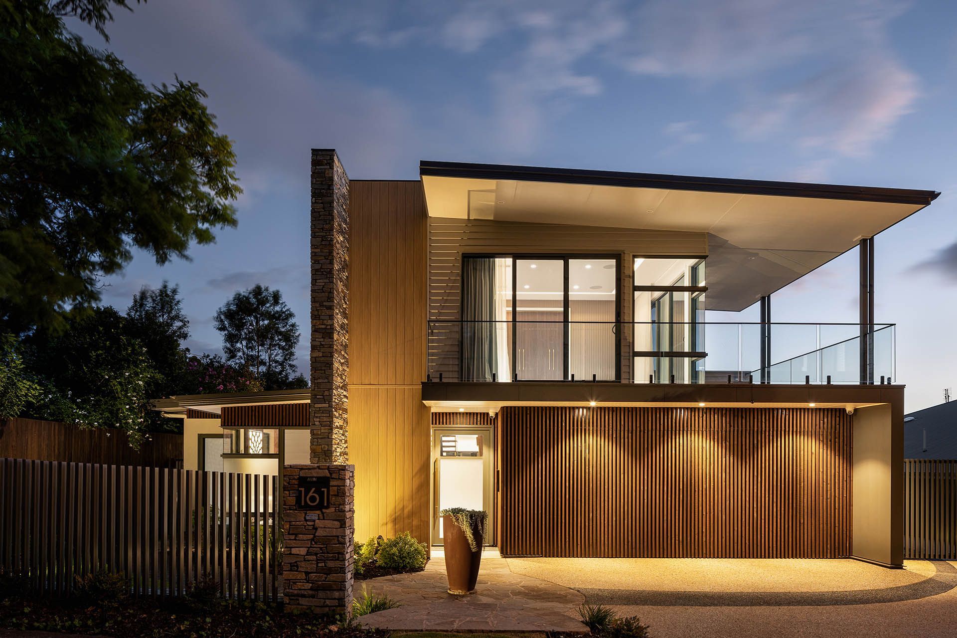Modern two-story house at dusk with warm wood facade, large windows, and a covered balcony