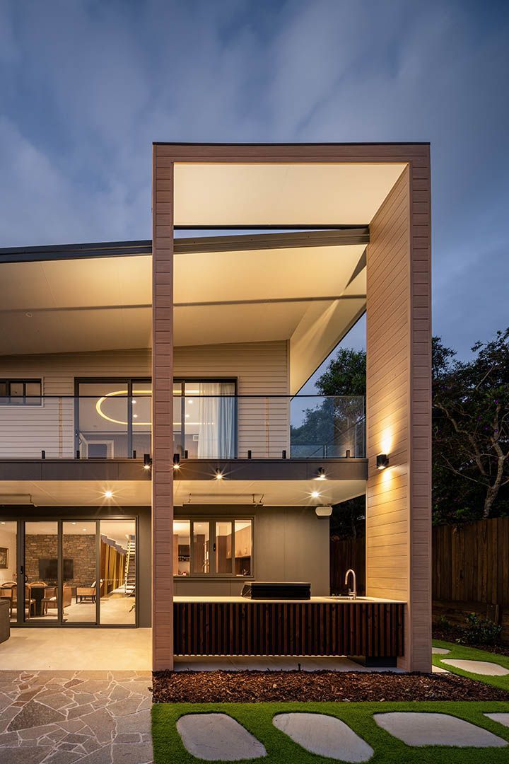 Modern two-story house with warm lighting, brick facade, and a large open-frame entrance at dusk