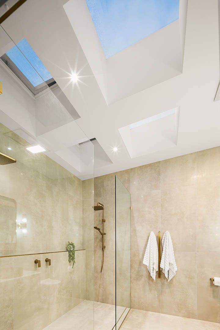 Modern shower with beige tile, glass enclosure, and skylights in a bright bathroom