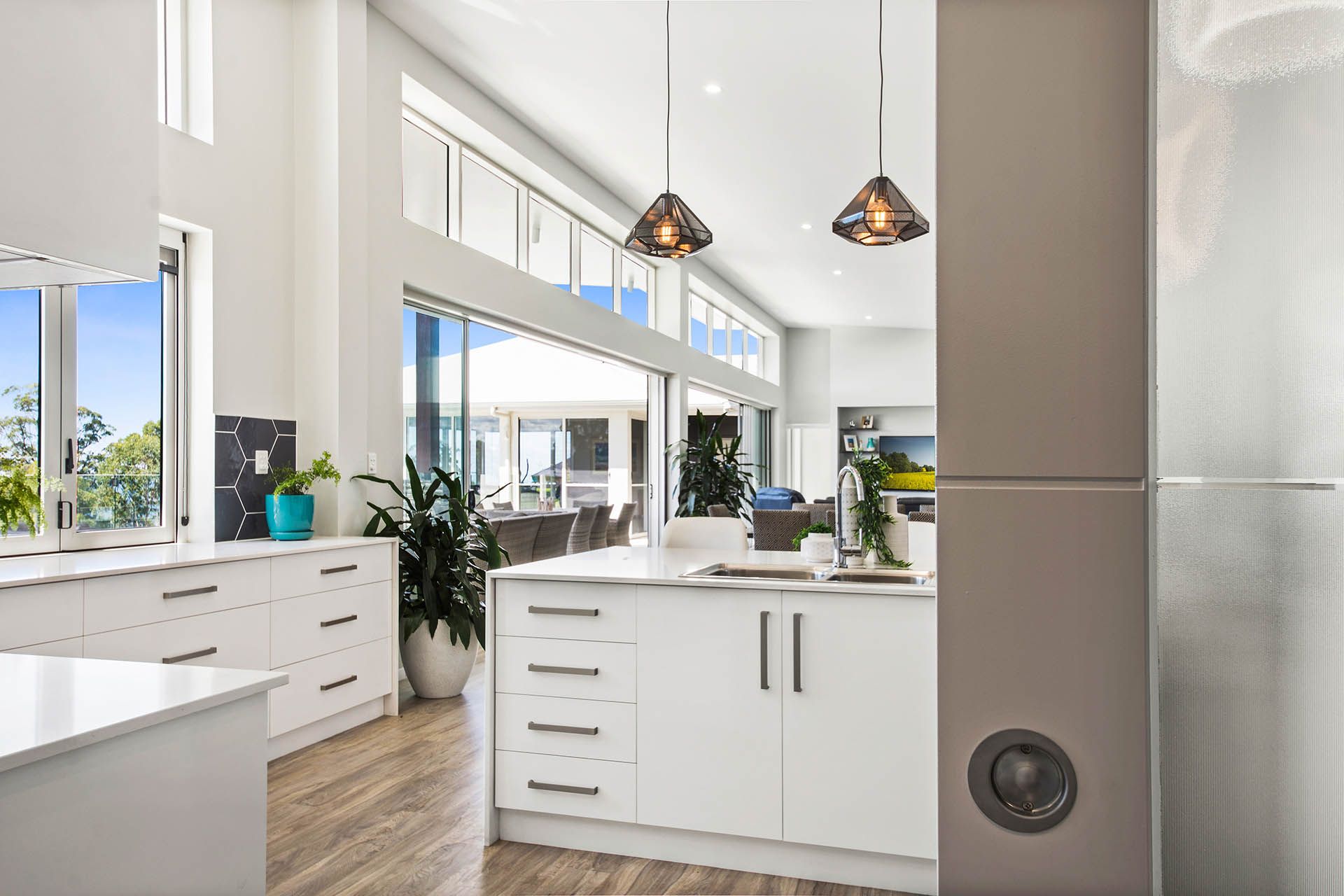 Bright modern kitchen with white cabinets, large windows, island, and pendant lights