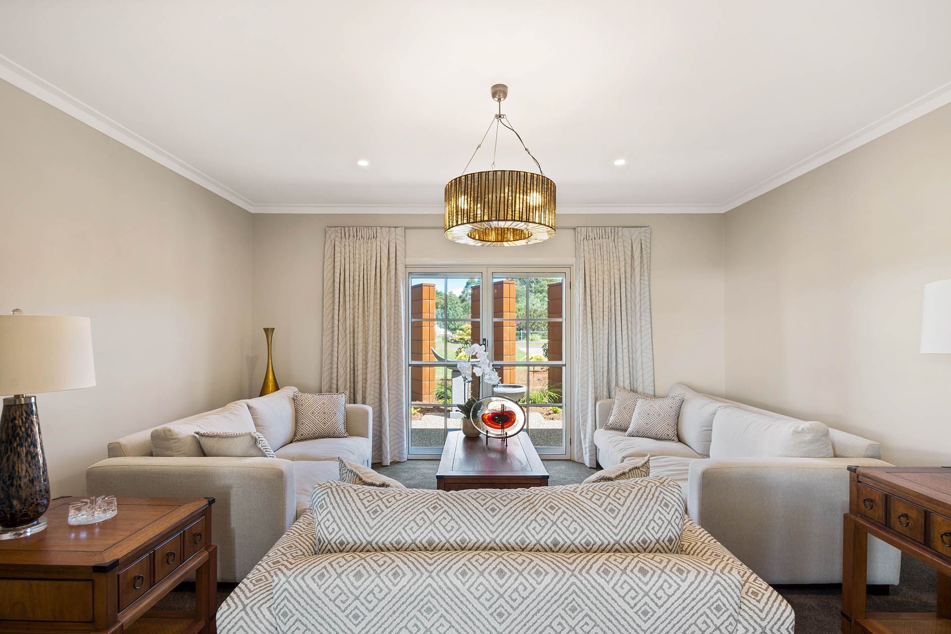 Bright living room with cream sofas, chandelier, and large windows opening to a garden.