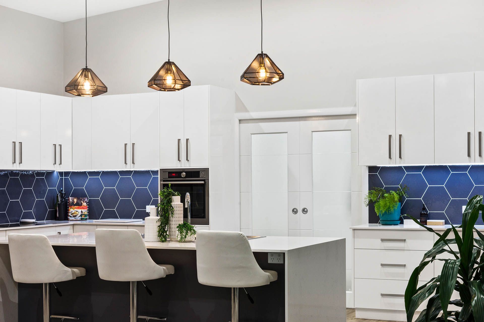 Modern white kitchen with blue tile backsplash, island seating, and pendant lights