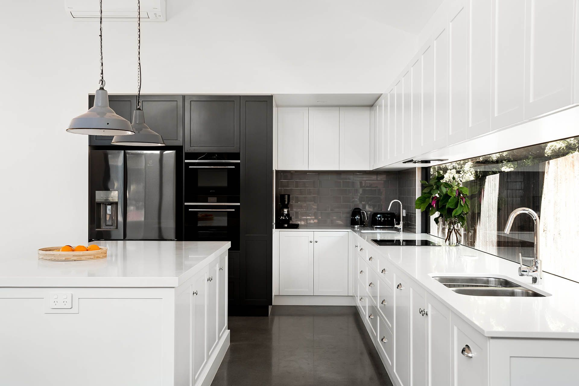 Bright white modern kitchen with black appliances, island, and sunlight by the sink