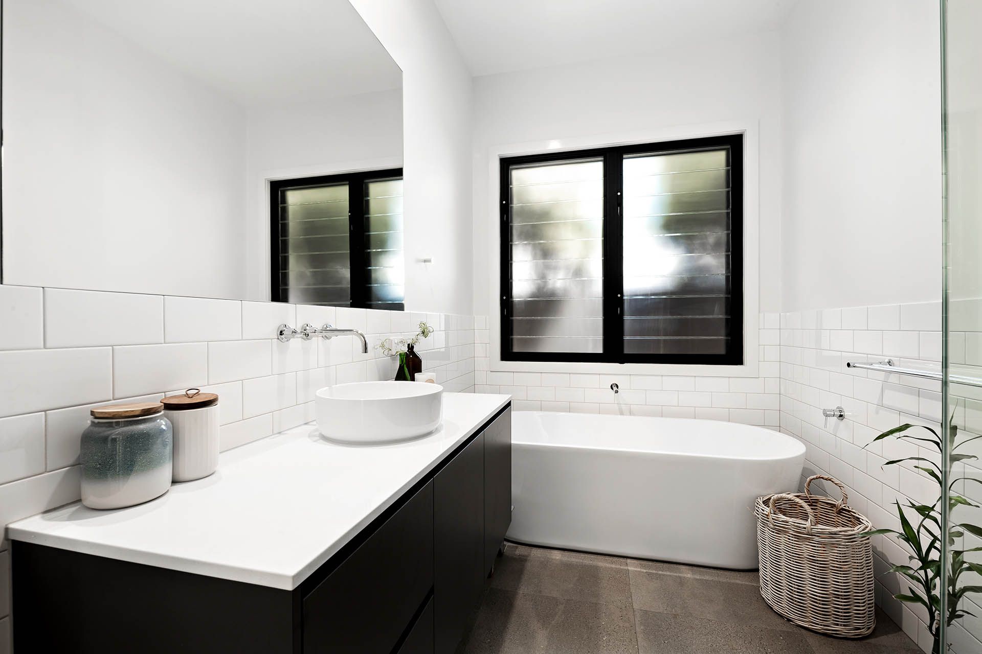 Modern white bathroom with a black vanity, freestanding tub, and two black-framed windows