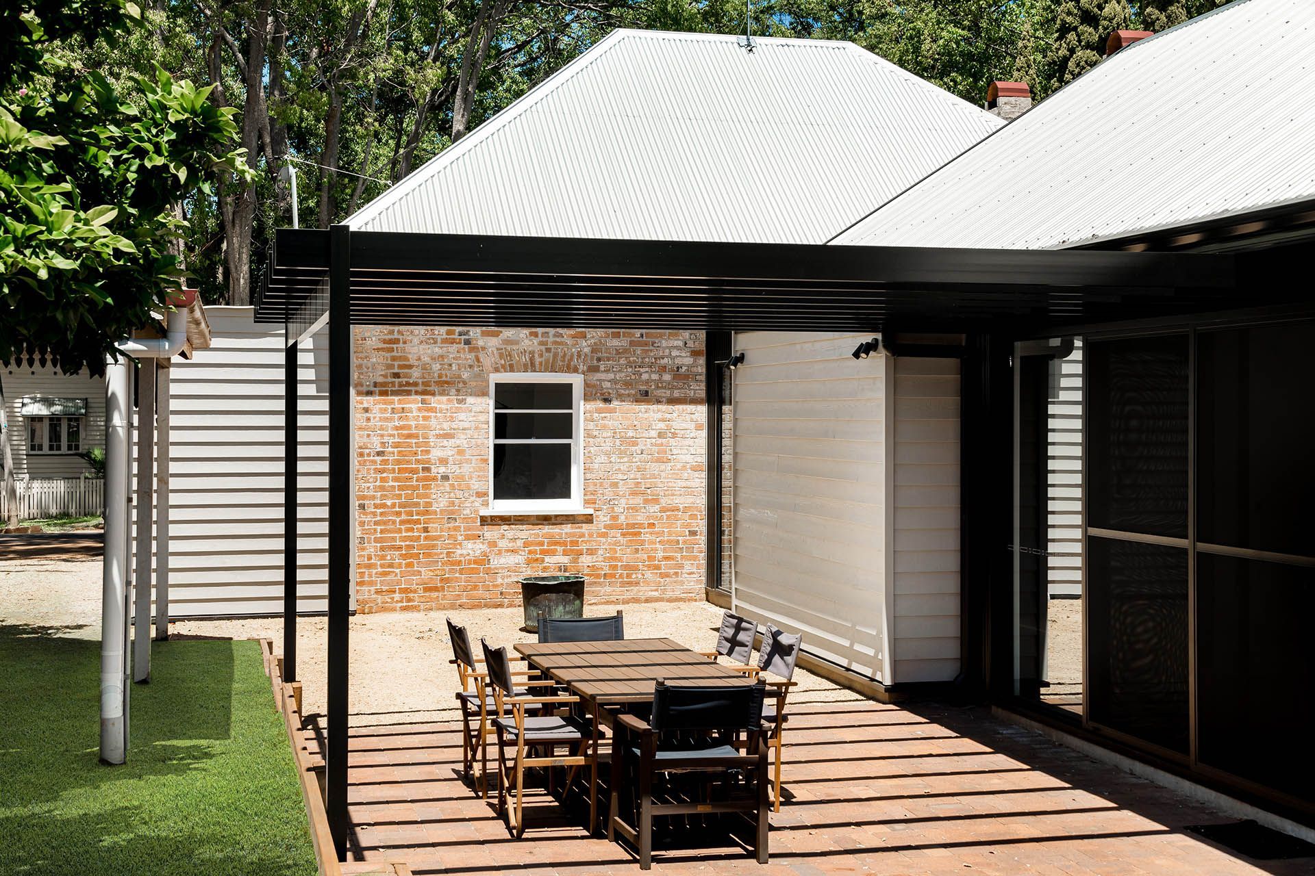 Patio with wooden dining table and chairs beside a brick house and covered outdoor area