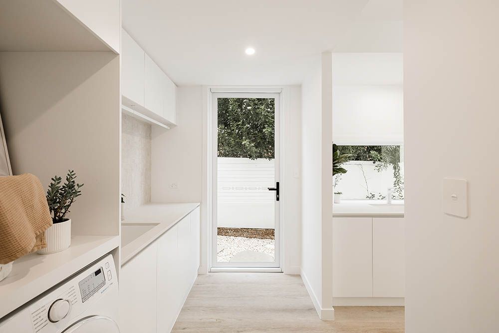 Bright minimalist laundry room with white cabinets and a doorway to a patio.
