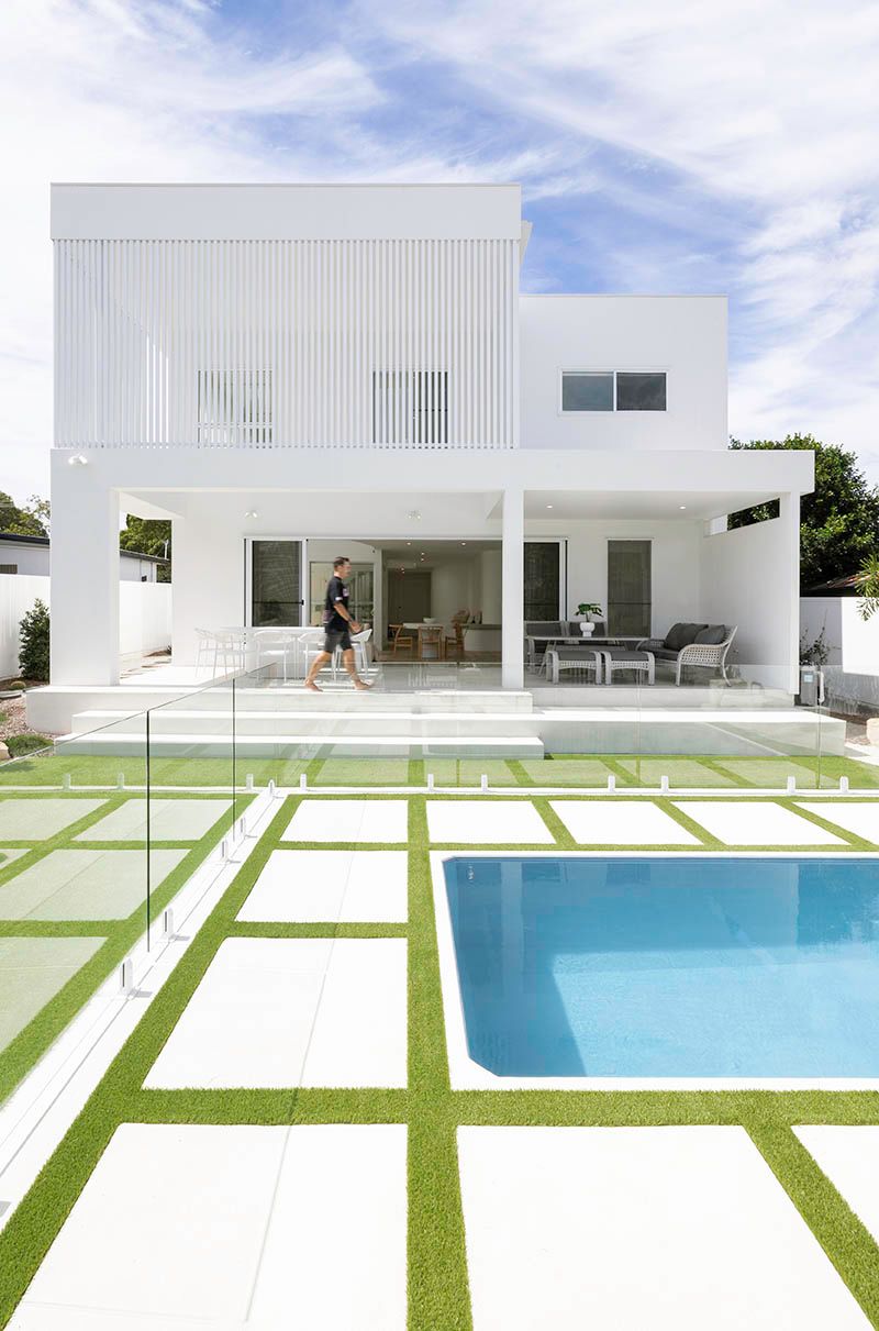 Modern white house with patio and blue swimming pool in a bright landscaped yard