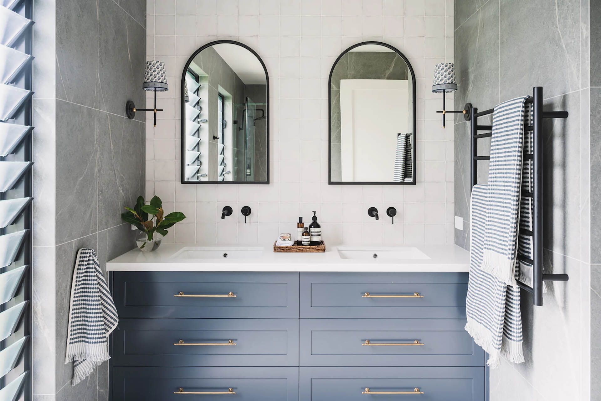 Bright bathroom vanity with blue cabinets, white countertop, arched mirrors, and striped towels