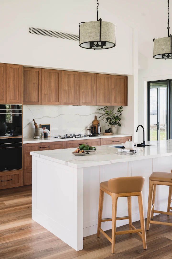 Modern kitchen with white island, wood cabinets, and two stools near a black faucet
