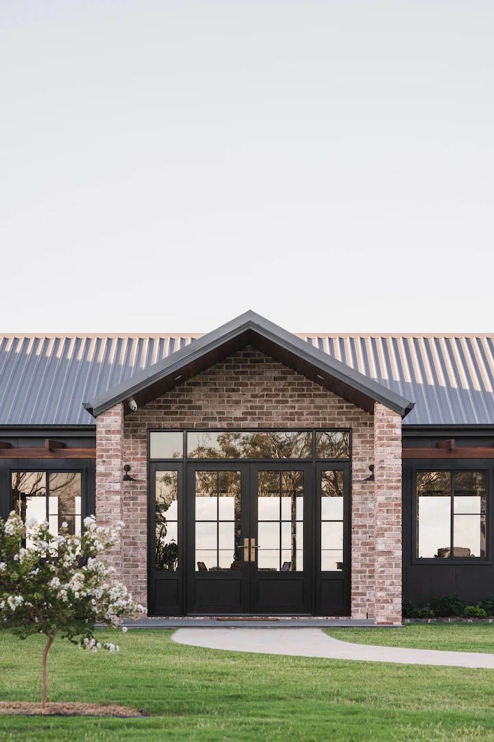 Brick building entrance with black double doors and a metal roof, fronted by grass and a walkway