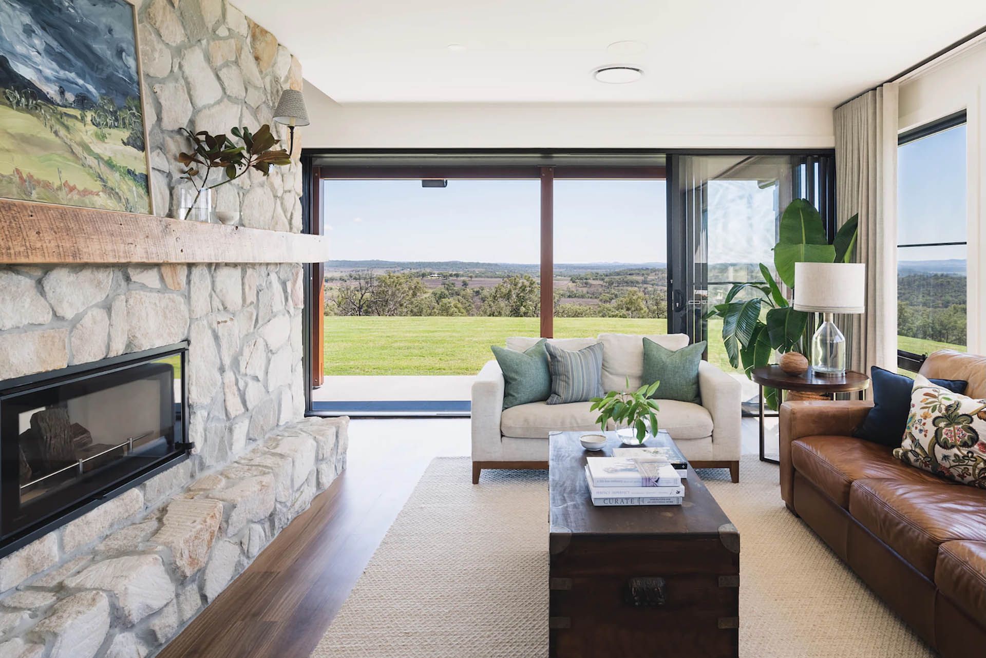Modern living room with stone fireplace, sofa, and open view to a bright green landscape