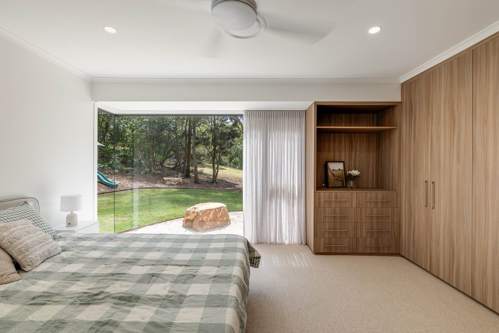 Modern bedroom with plaid bed, wood closet, and large sliding glass door to a green backyard