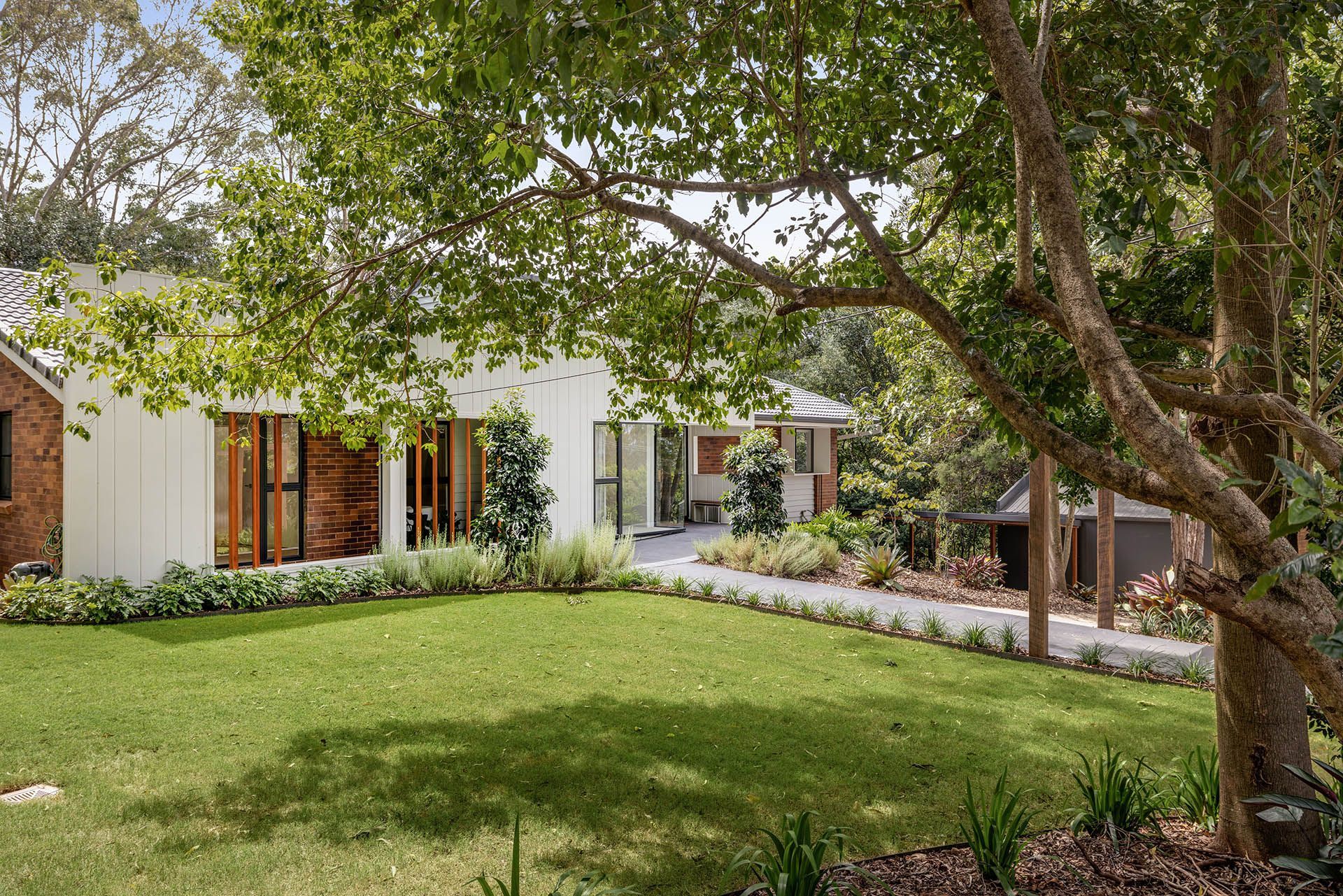 Modern house with white exterior, large windows, and a green front lawn shaded by trees