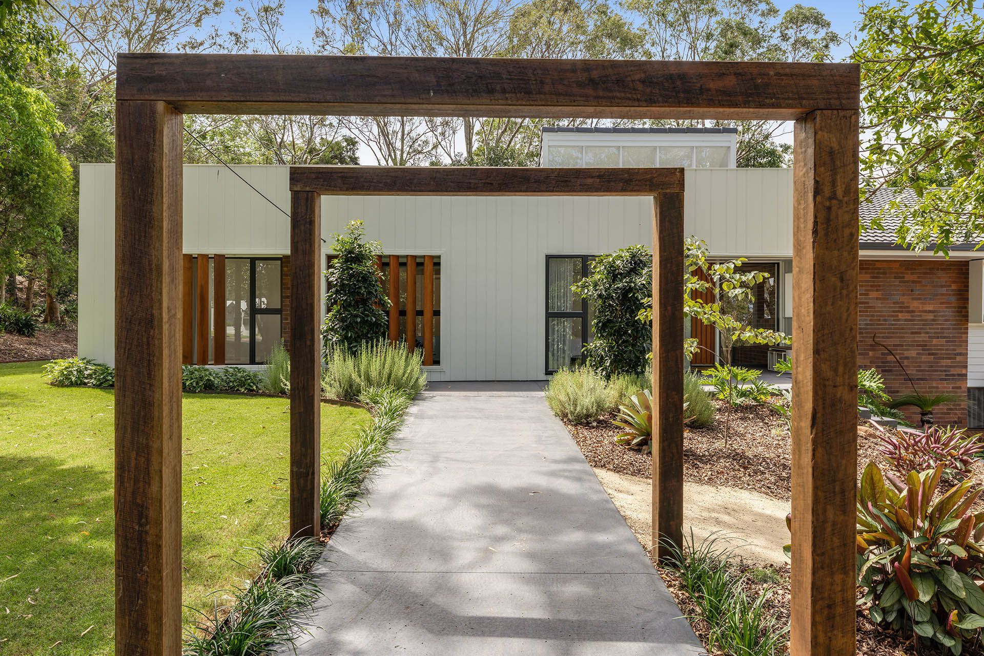 Modern house entrance with a concrete path framed by wooden pergolas and landscaped greenery
