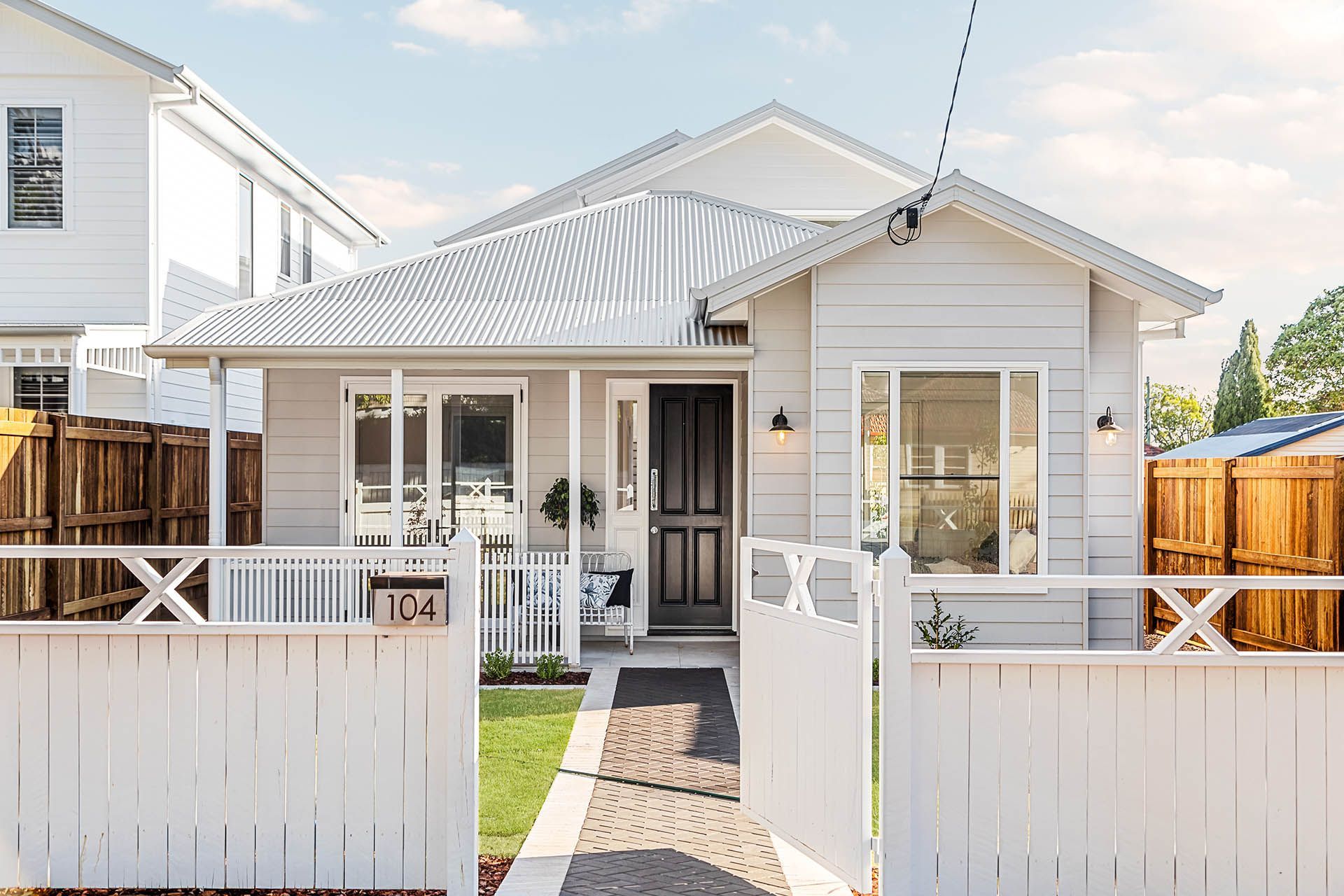 Small white house with a front porch, white fence, and paved walkway under a clear sky