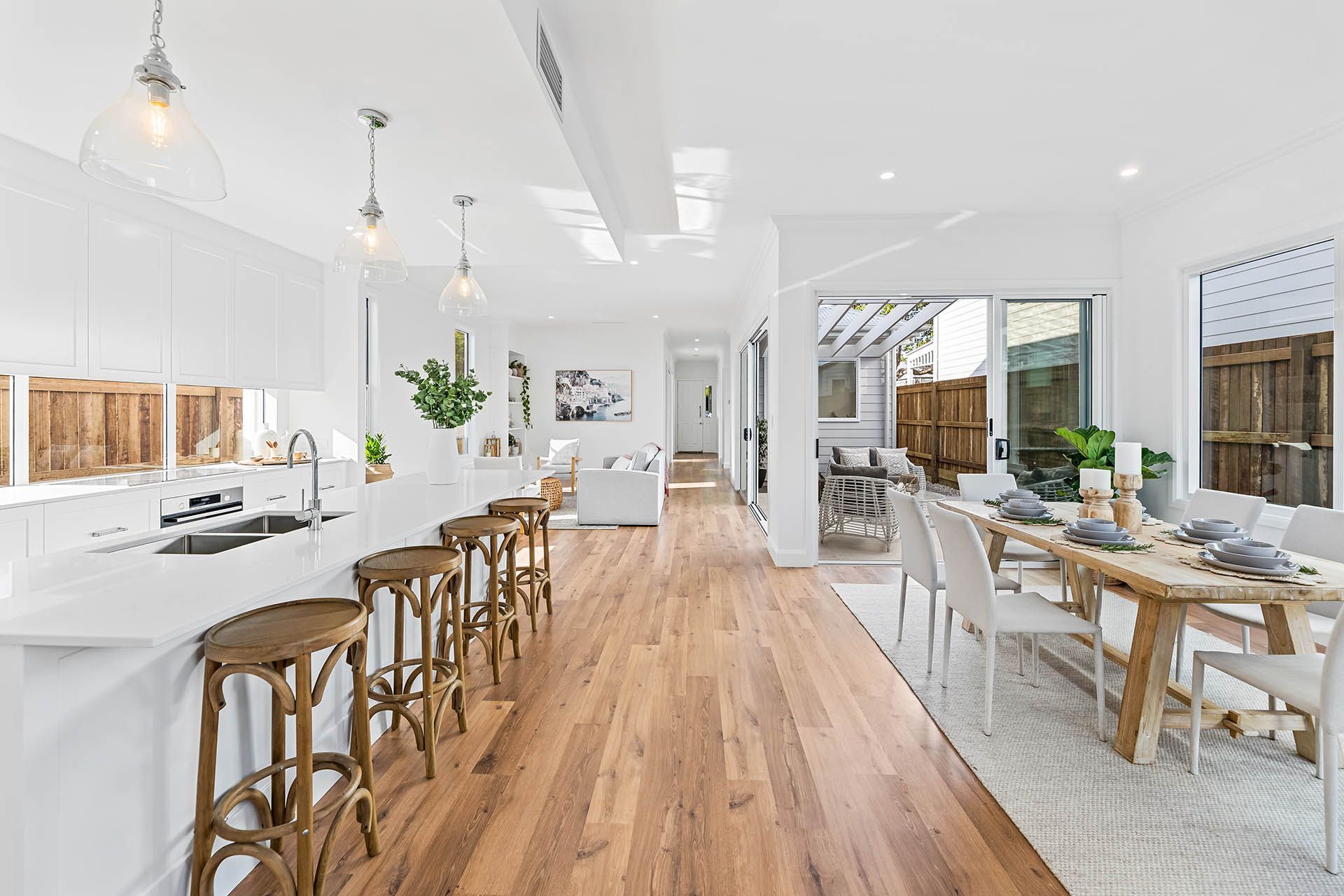 Bright white café interior with wooden tables, stools, and a long central aisle under pendant lights