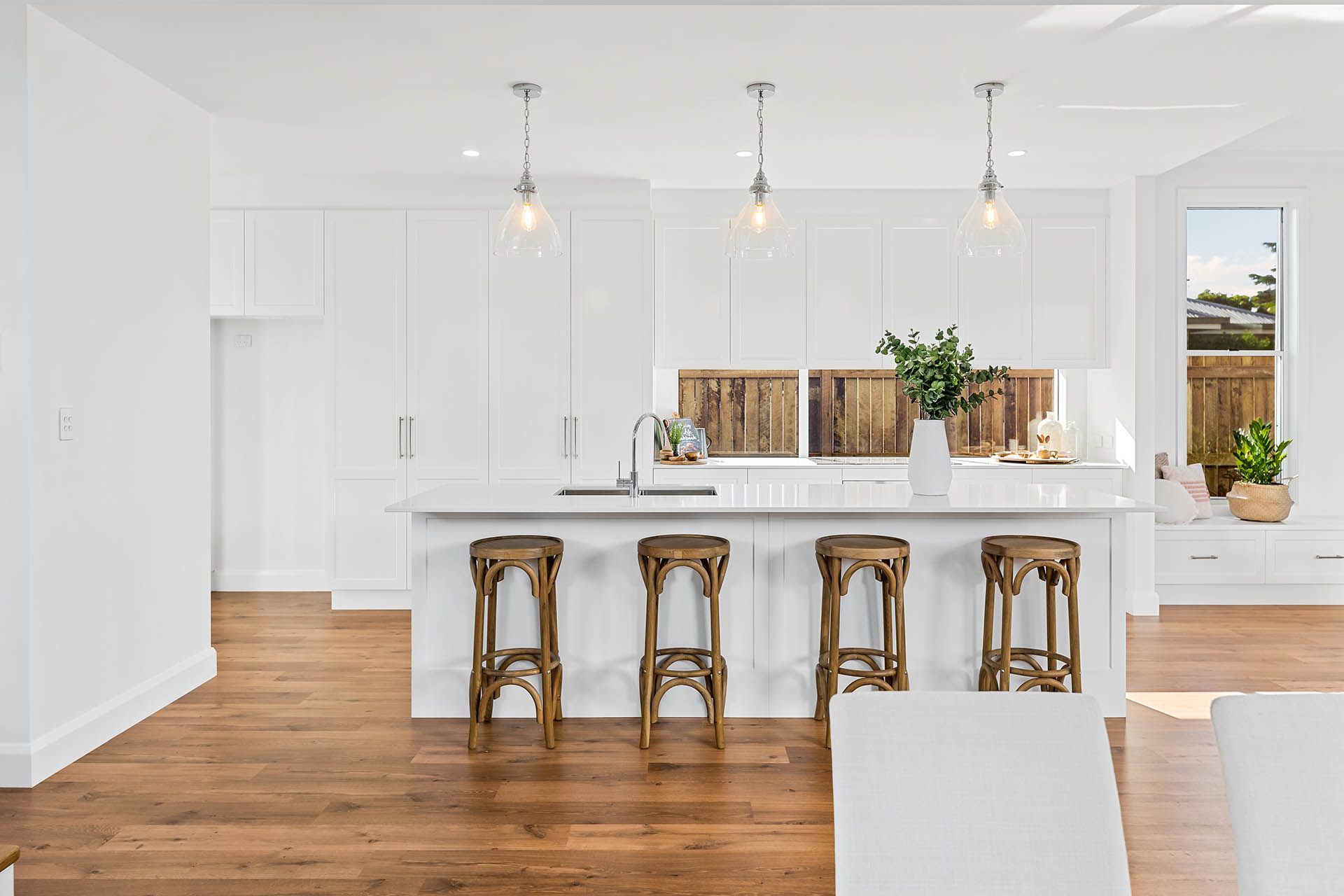 Bright modern kitchen with white cabinets, wood floors, island stools, and pendant lights