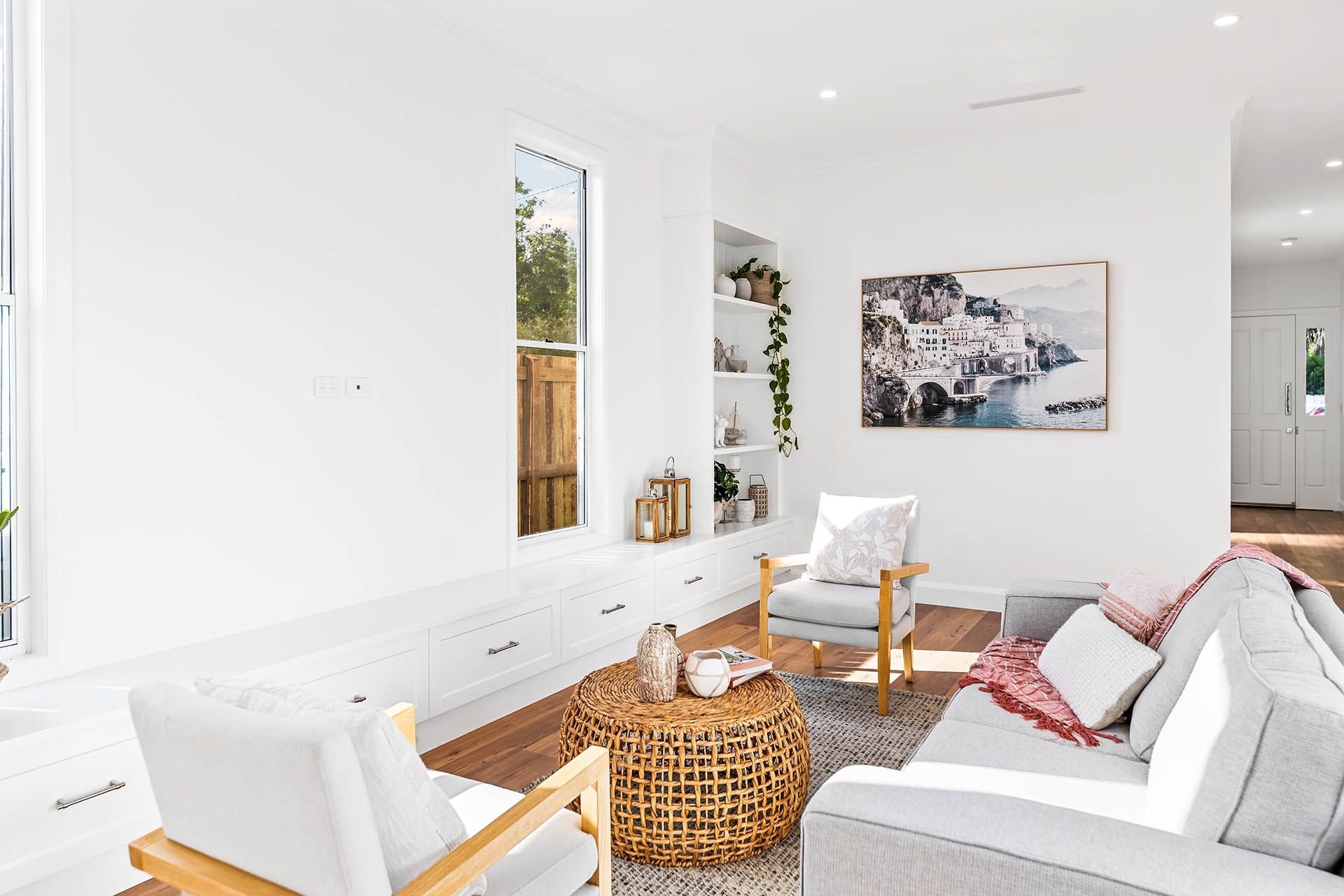 Bright living room with white walls, gray sofa, wicker table, armchair, and wall art