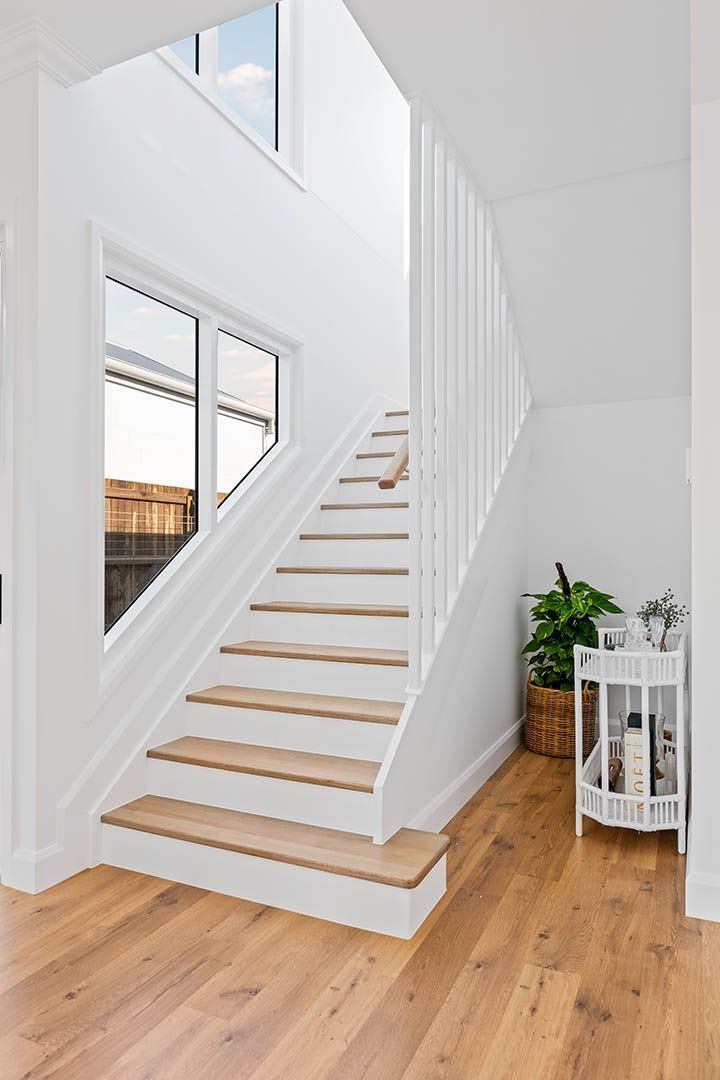 Bright white staircase with wooden treads in a minimalist hallway beside a potted plant and window.