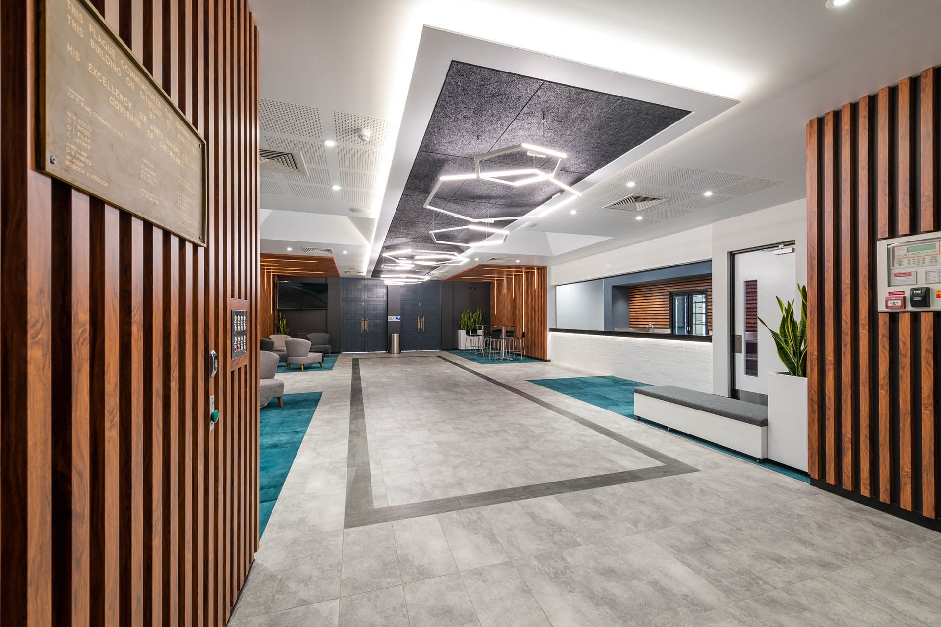 Modern hotel lobby with wood slat walls, white ceiling, gray floor, and turquoise accents