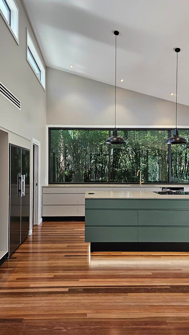 Modern kitchen with wood floors, mint island, white cabinets, and large window overlooking trees