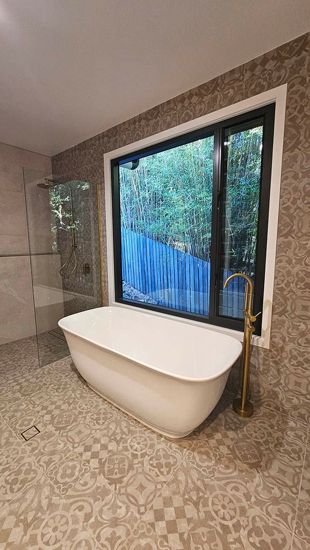 Modern bathroom with a freestanding tub beside a large window and patterned tile floor.