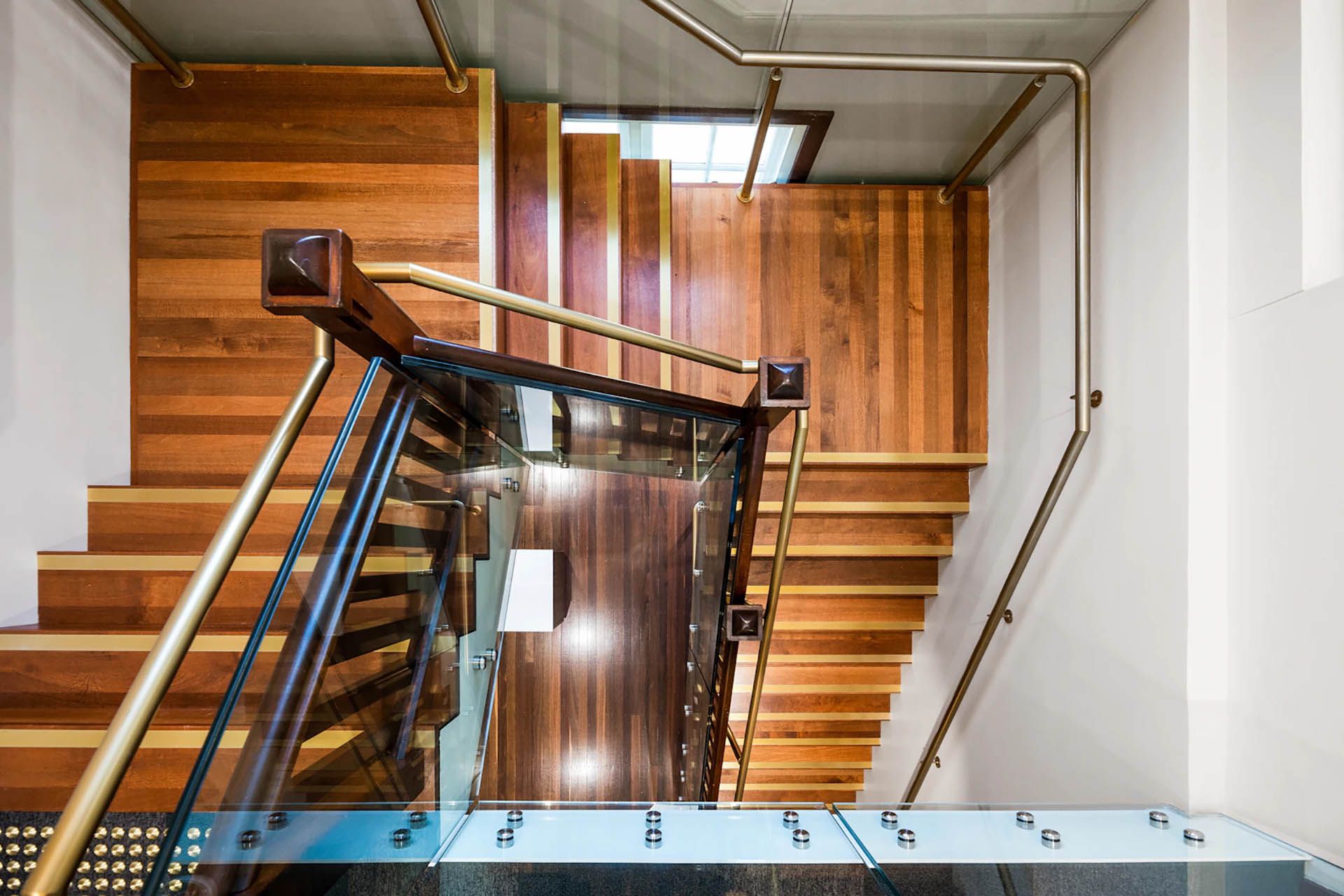Wooden stairwell with a central landing and polished handrails, viewed from above.
