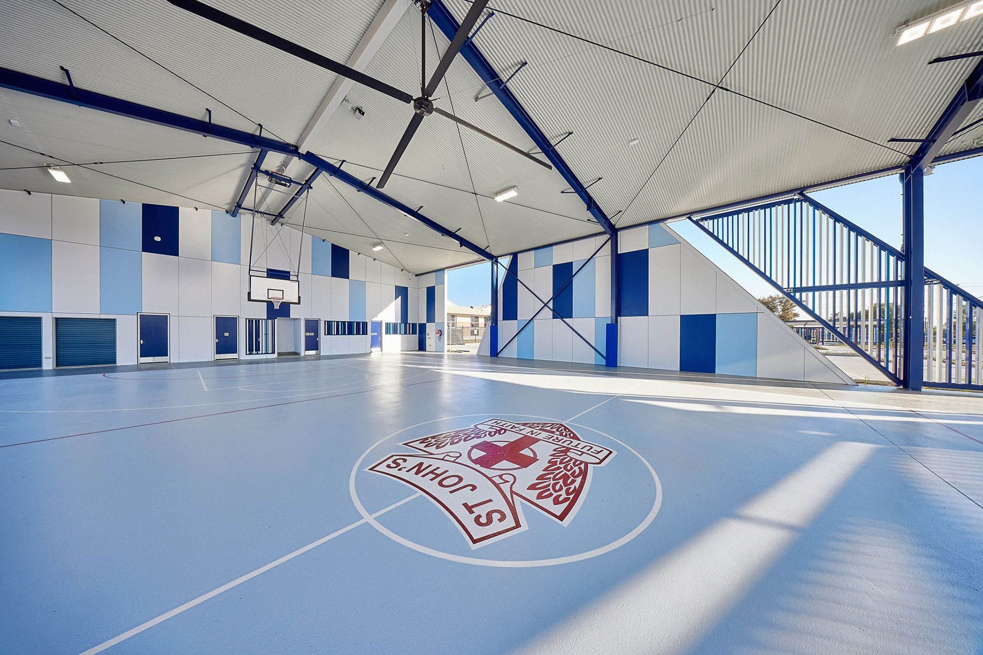 Indoor sports court with blue floor, white-and-blue walls, and a red center logo under a curved roof