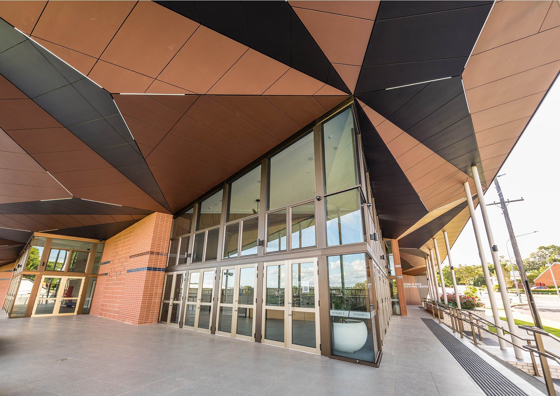 Modern building entrance with glass doors and angular copper and black canopy.