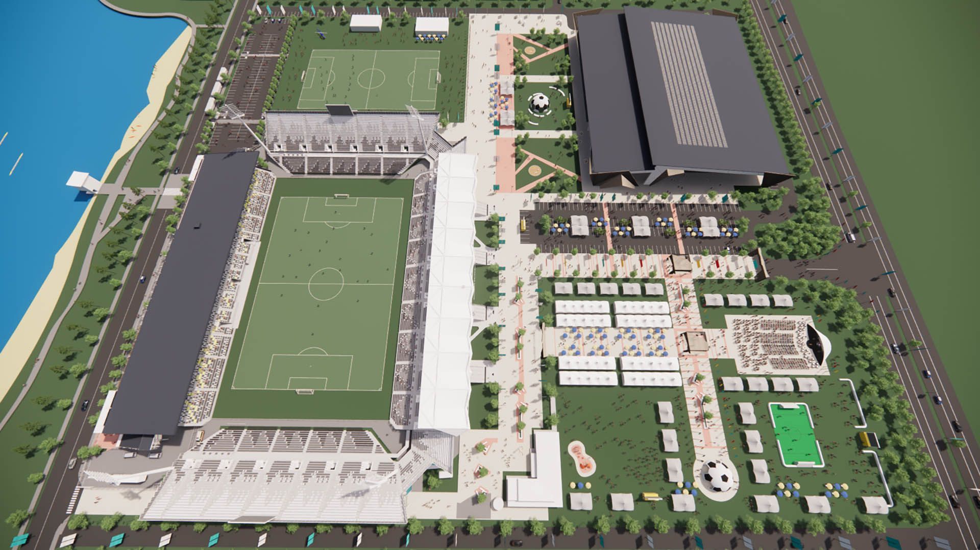 Aerial view of a sports complex with a soccer field, large gymnasium, parking lots, and nearby waterfront.