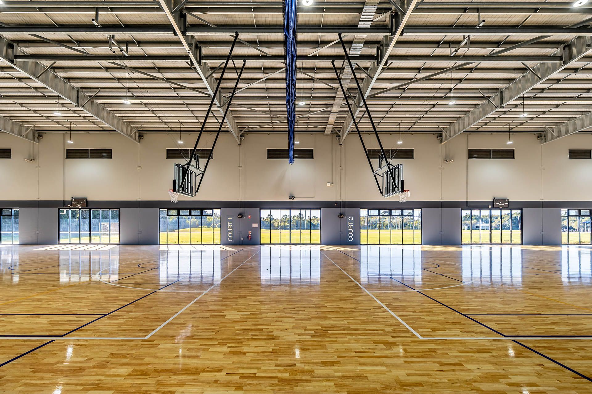 Empty indoor basketball gym with polished wooden floor and folded hoops under a high metal ceiling