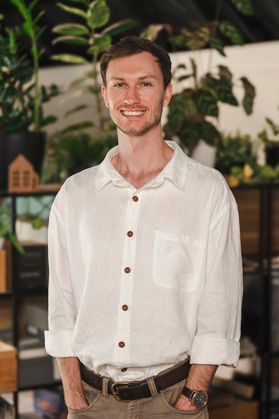 Smiling man in a white shirt standing indoors with plants in the background