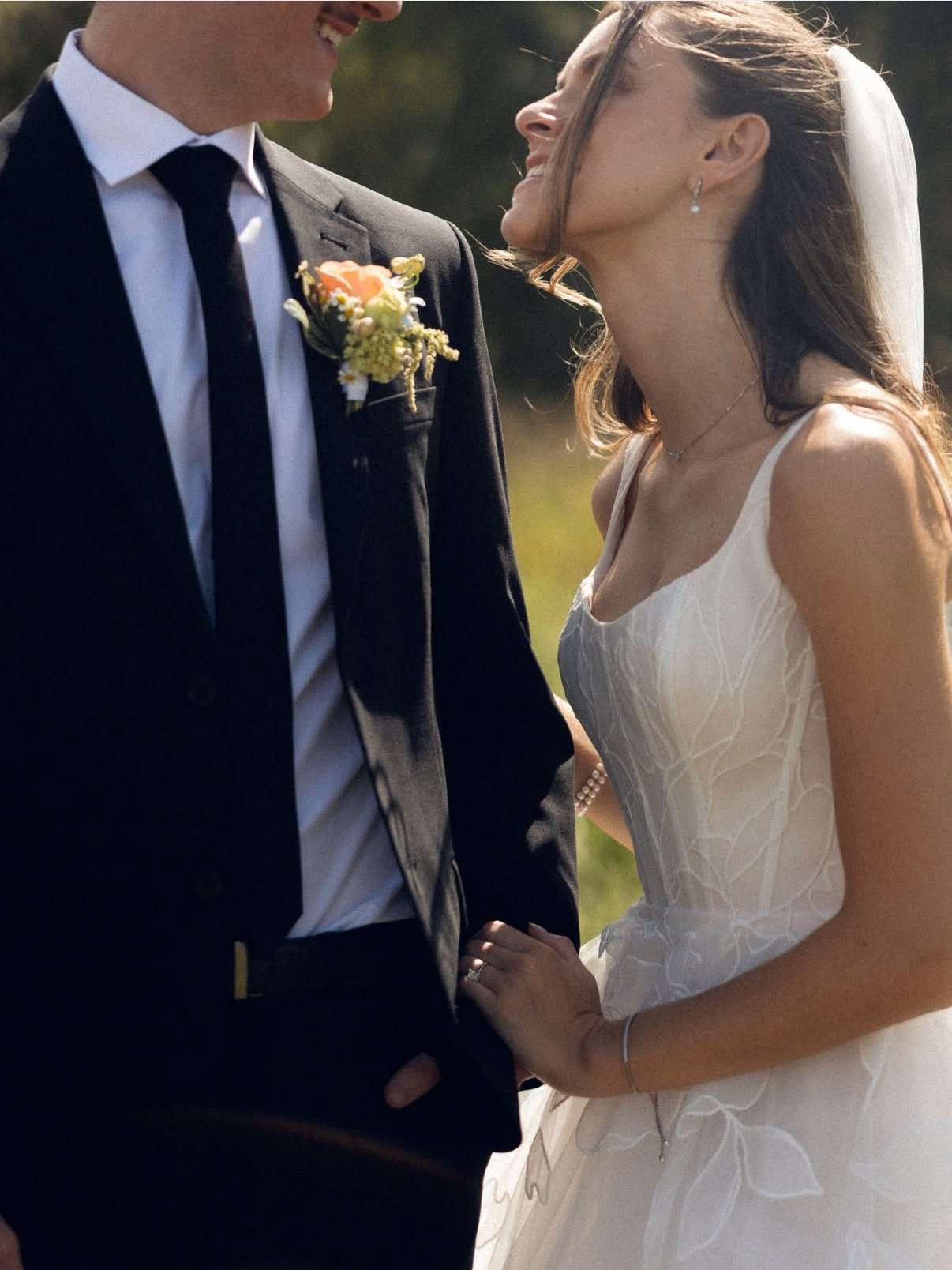 Bride and groom smiling at each other, holding hands. The groom wears a black suit, and the bride is in a white dress