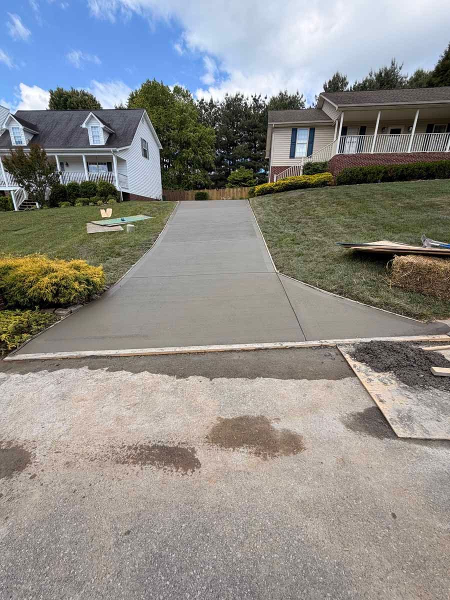 Concrete sidewalk leading uphill between houses with a grassy slope and cloudy sky