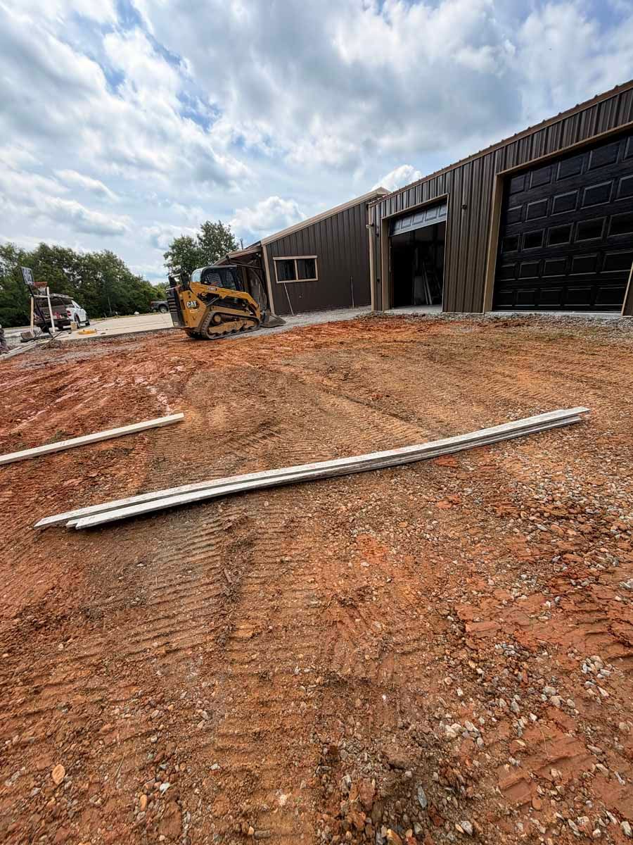 Construction site with excavator beside a long building and dirt-covered ground