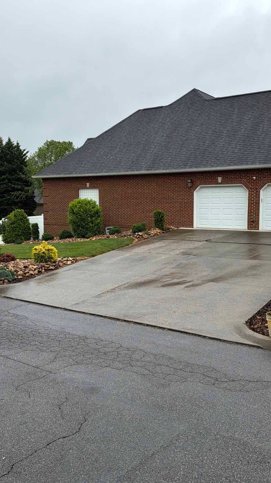 Brick suburban house with a dark shingled roof, white garage door, and sloped driveway on a cloudy day