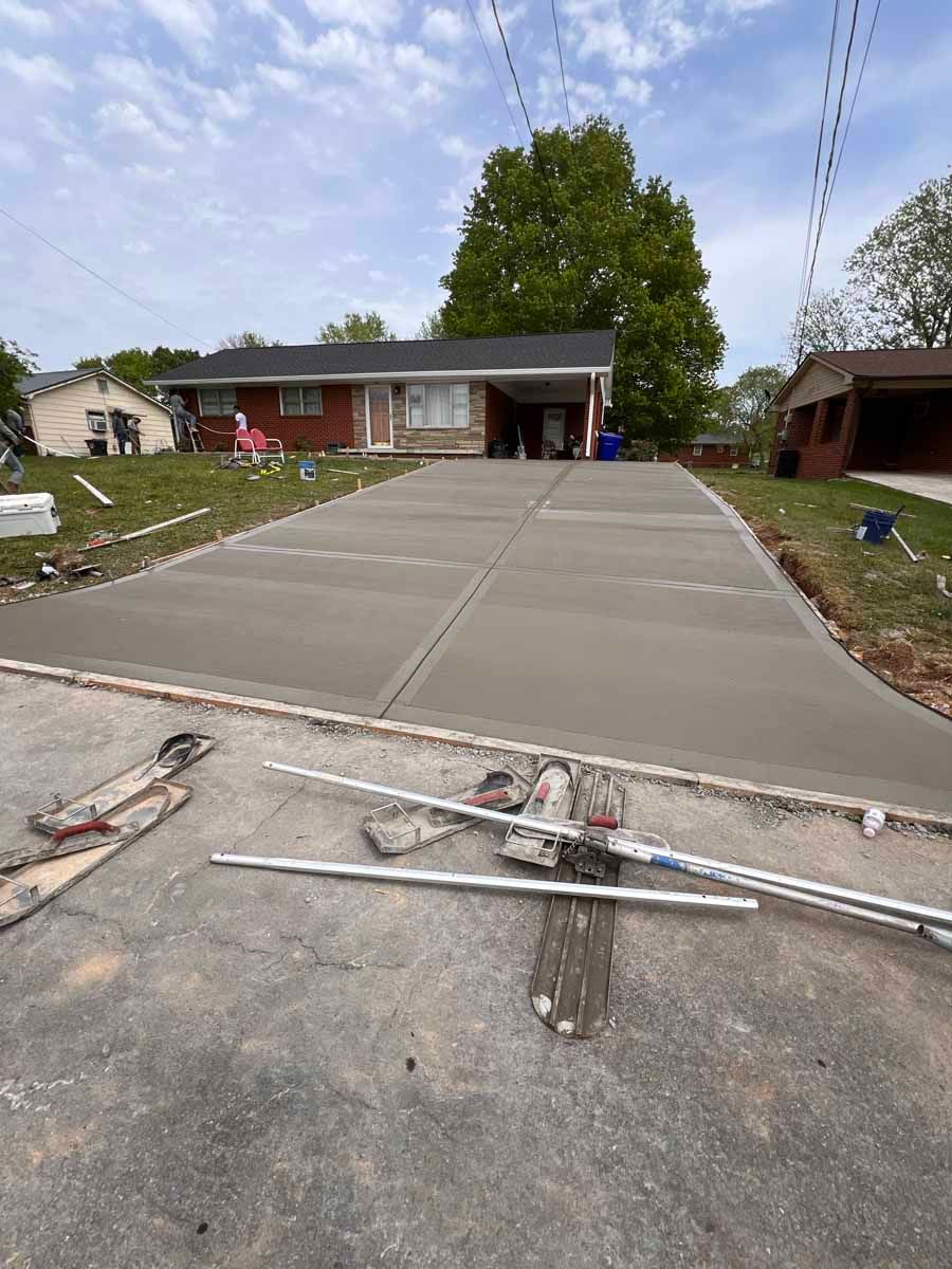 Fresh concrete driveway leading to a single-story house, with construction tools in the foreground.