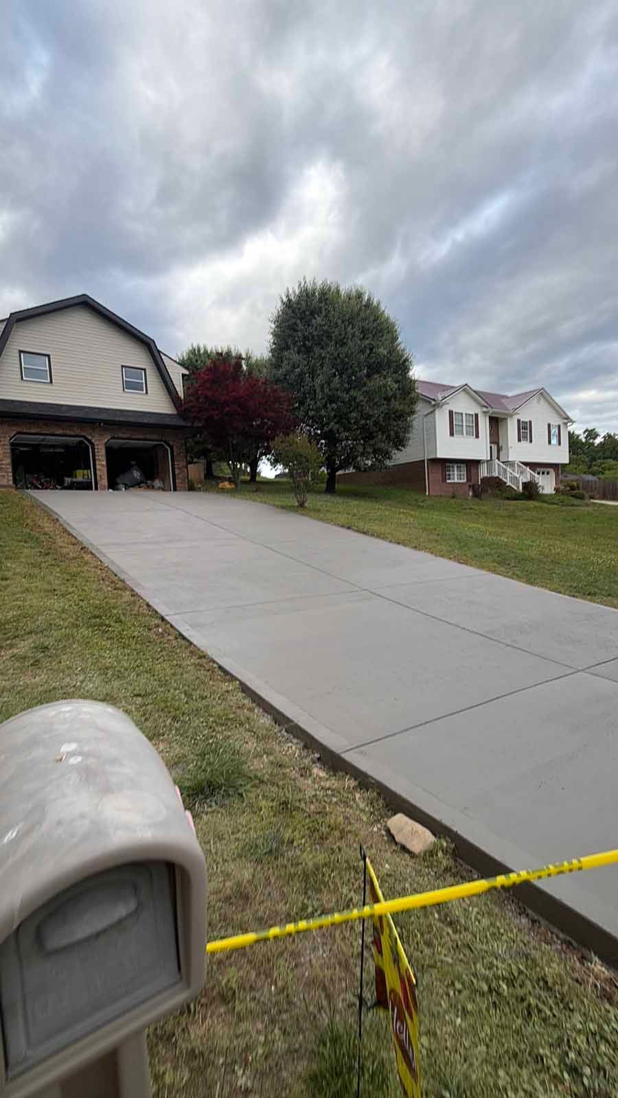 Suburban house with long concrete driveway under cloudy sky, yellow caution tape across the front yard.