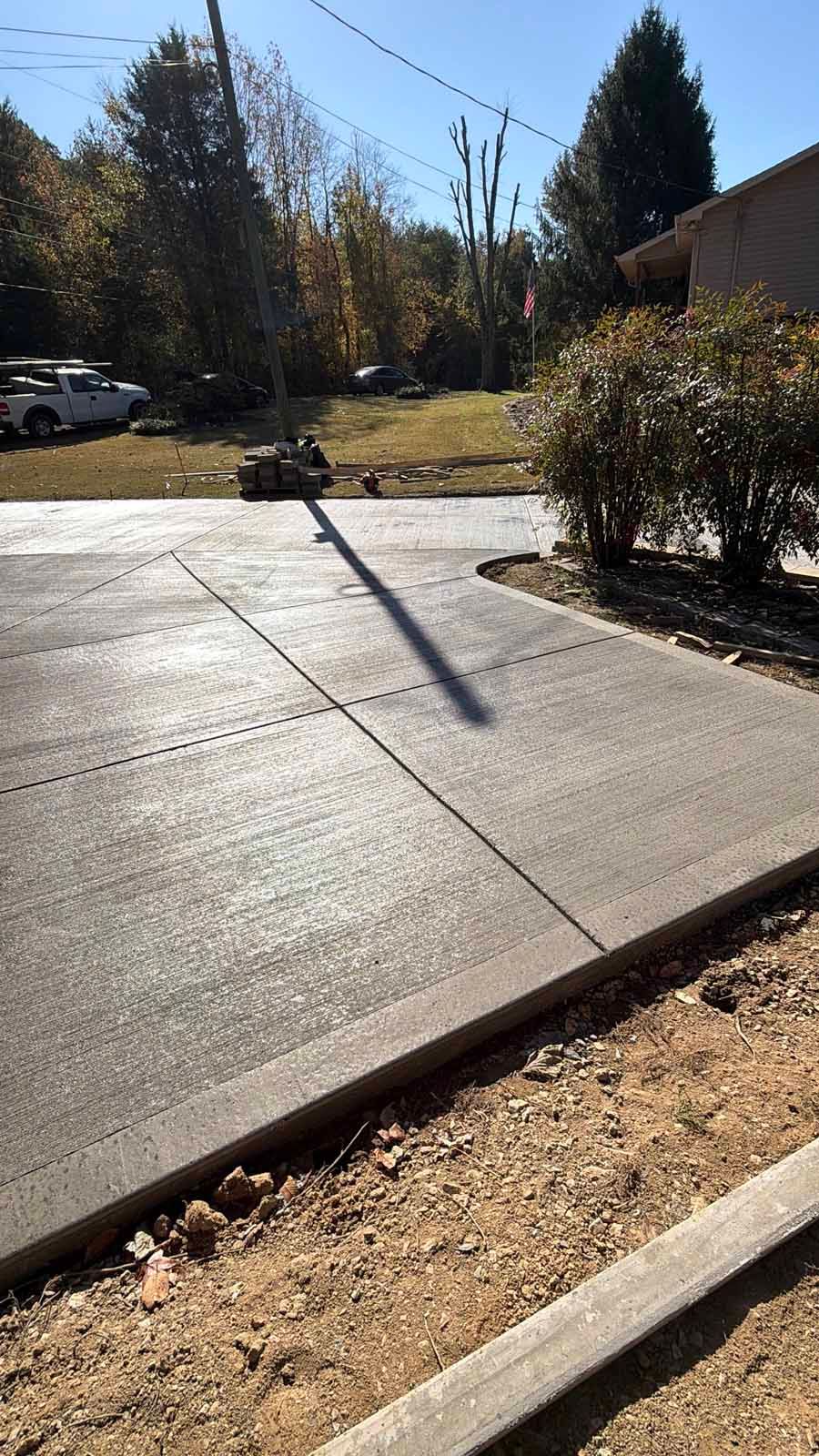 Concrete driveway beside a curb and shrubs, with trees and parked cars in the background.