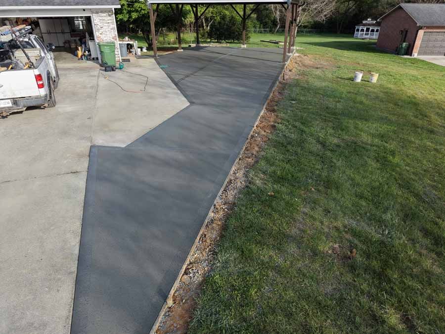 Freshly poured concrete driveway beside a grassy lawn and house garage area