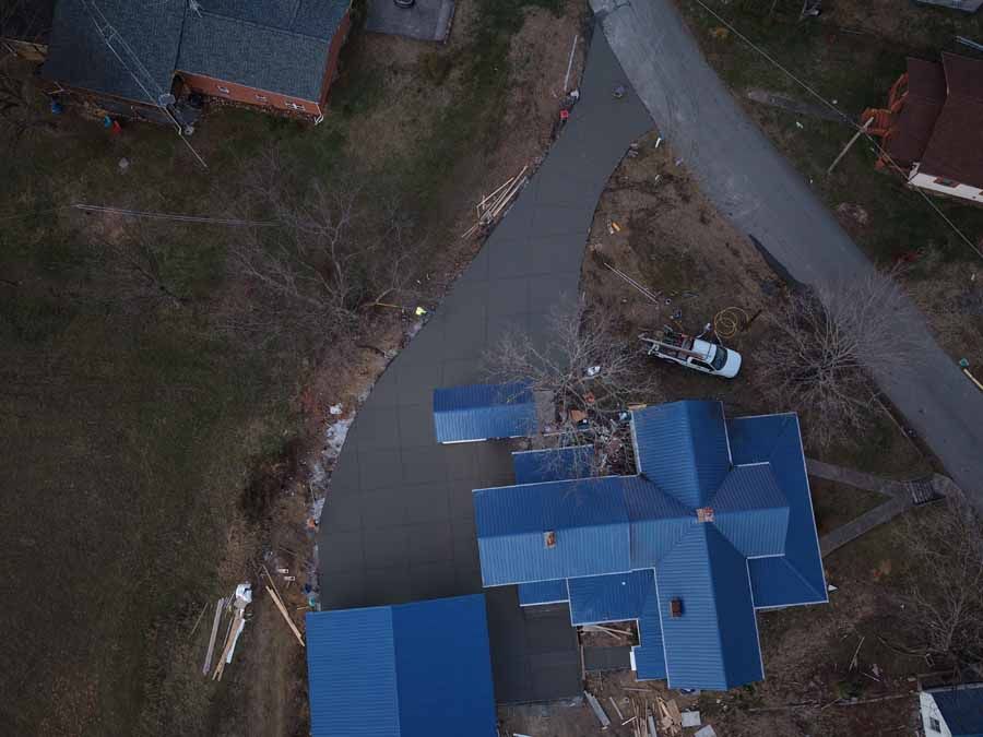 Aerial view of blue-roofed buildings beside a curved road and surrounding bare ground.