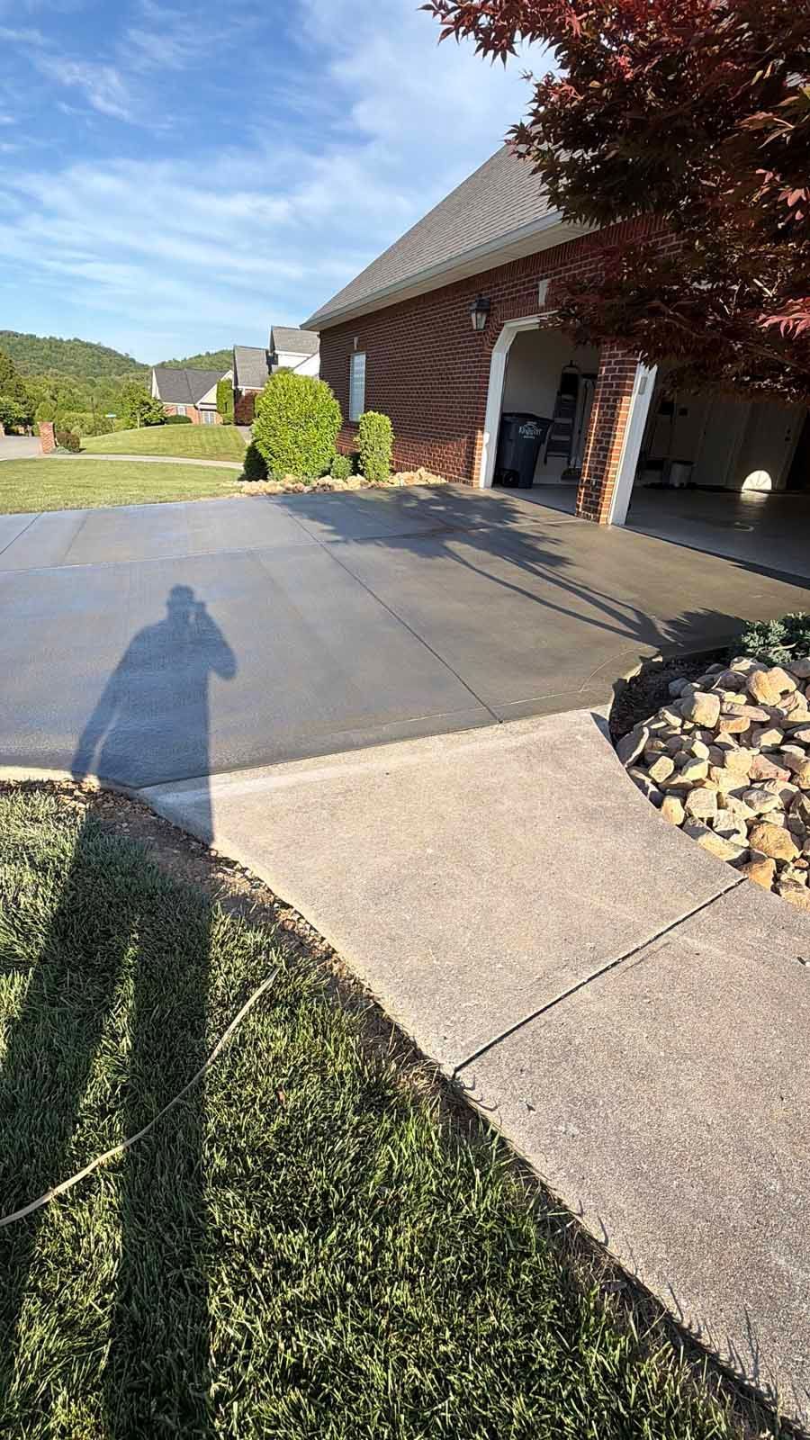 Driveway beside a brick house with an open garage, lawn, and long shadow at sunset