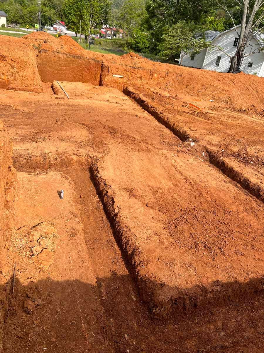 Terraced orange dirt excavation site with stepped trenches and a few trees in the background