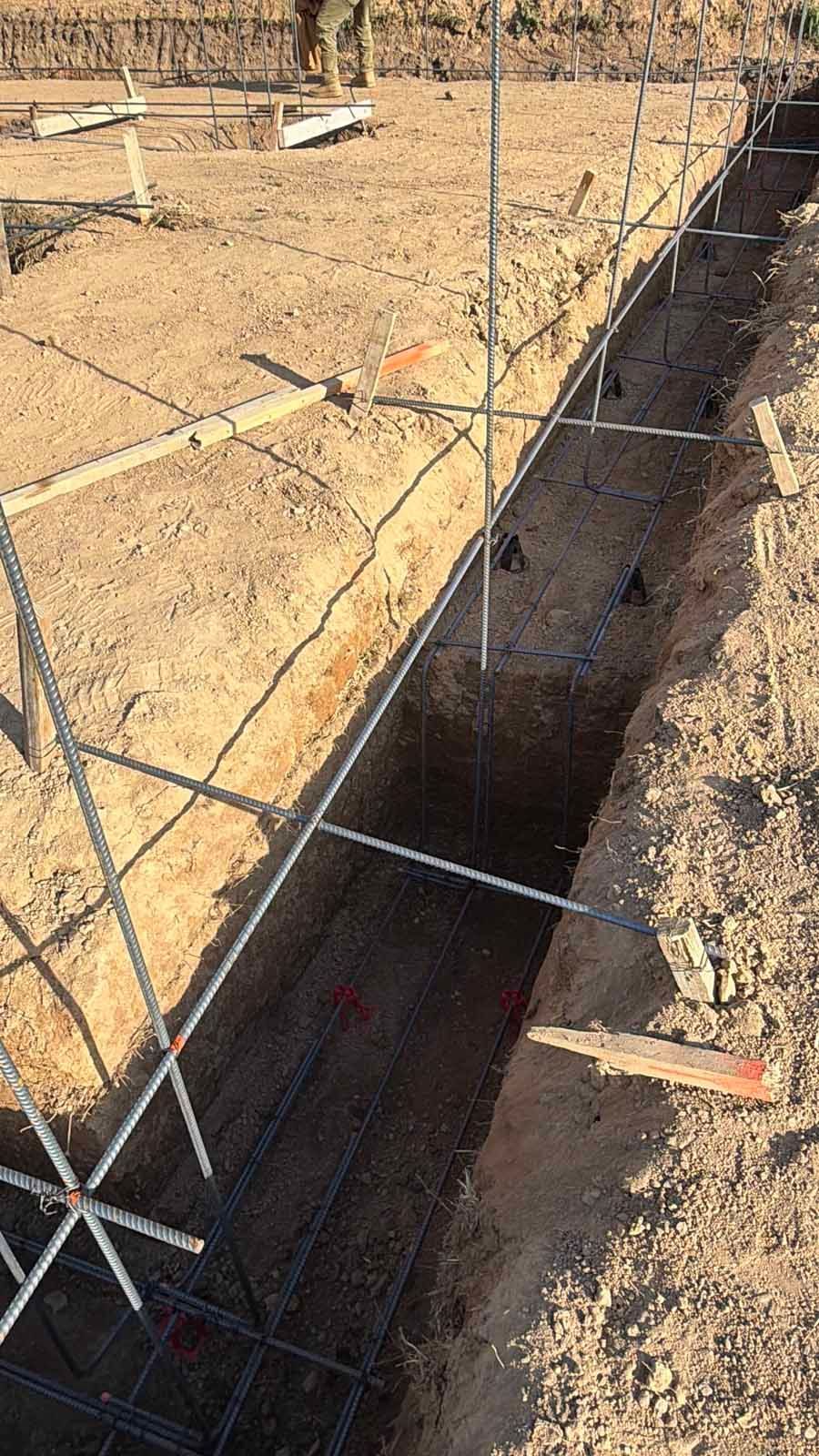 Rebar cage in a narrow concrete trench at a construction site, surrounded by dirt.