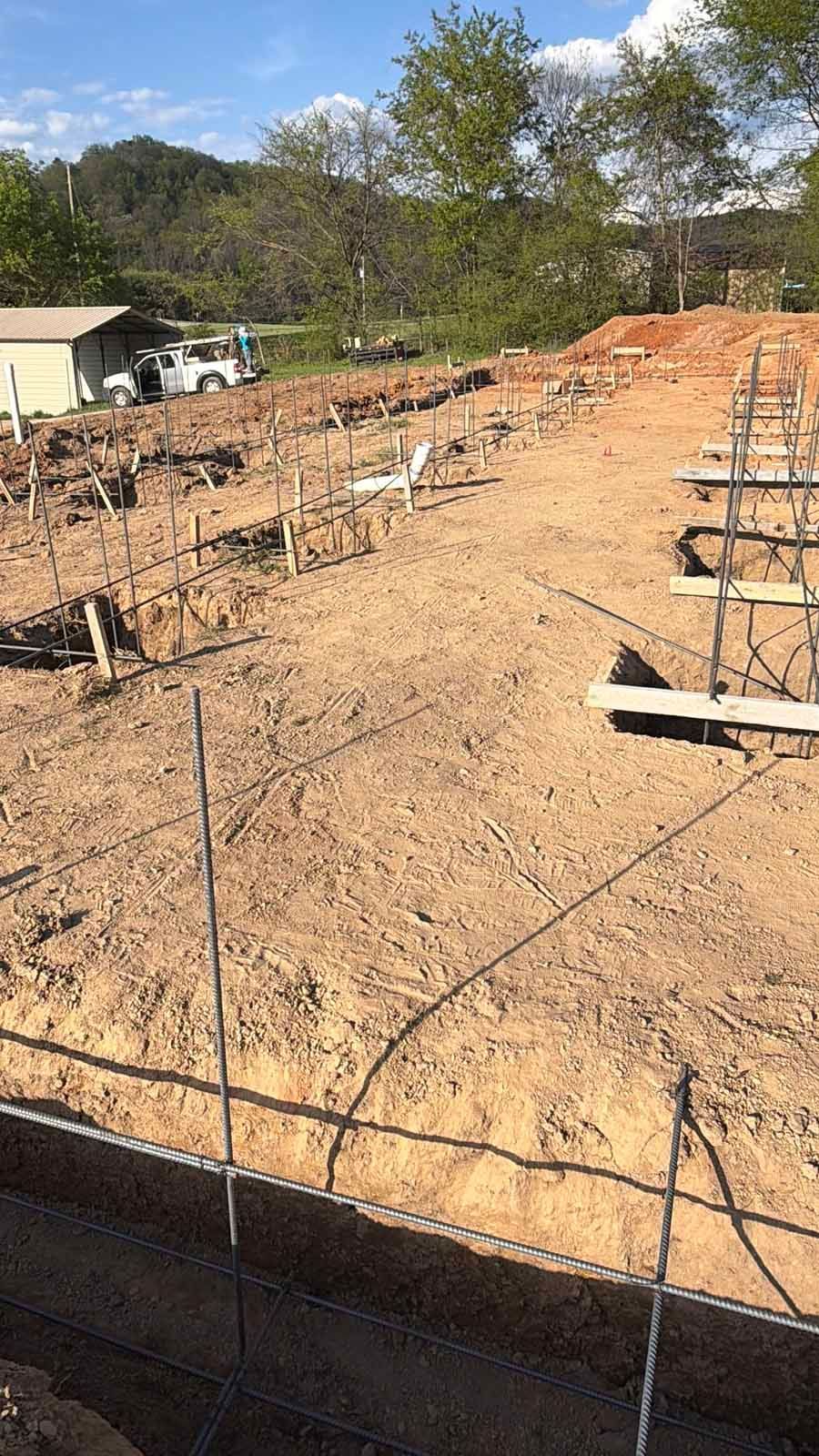 Construction site with foundation rebar and wooden forms on bare dirt under a blue sky